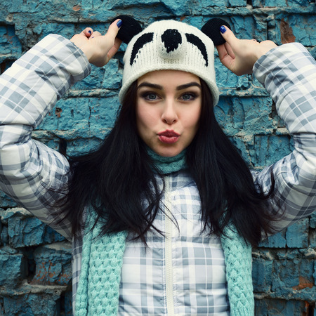 beautiful cool girl in funny hat gainst grunge brick wall make faces, tonedの写真素材