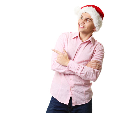 young cheerful christmas man with santa's hat pointing at copyspace over white backgroundの写真素材
