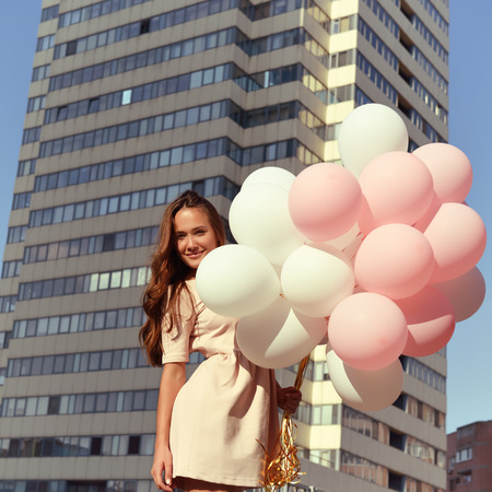 Beautiful young girl holding colored ballons over high-rise building. Urban teenage background. Toned.の写真素材