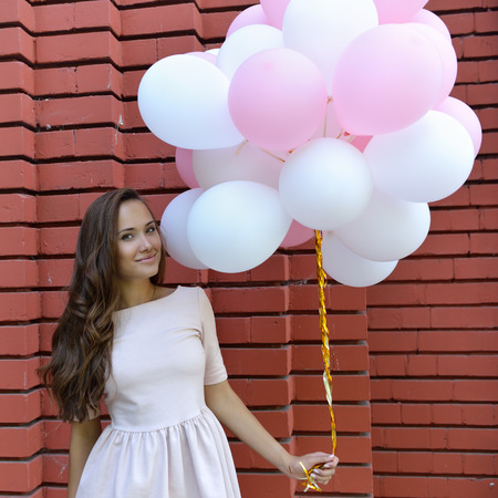 happy young woman standing over red brick wall and holding pink and white balloonsの写真素材