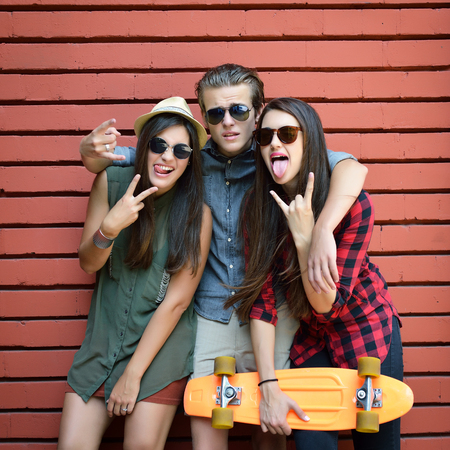 Young people posing with penny board and sun glasses against red brick wall. Urban lifestyle, happiness, joy, friends, teenage, first love concept. Image toned and noise added.の写真素材