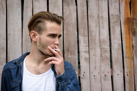 Young handsome man smoking outdoor against grunge obsolete fenceの写真素材