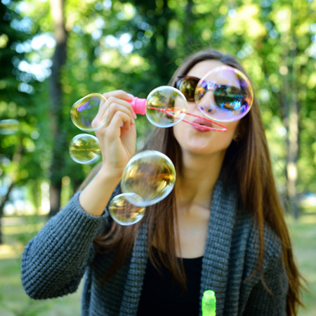 Young woman blowing soap bubbles outdoor in fall park. Image toned and noise added. Soft focus.の写真素材