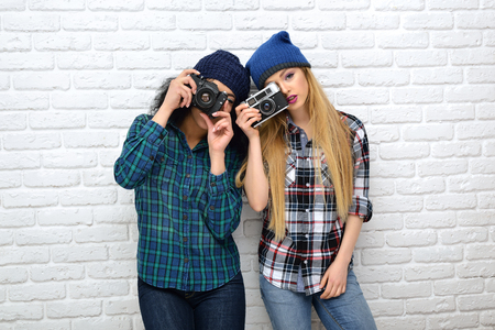Two hipster girls taking photo with retro cameras over white wall.の写真素材