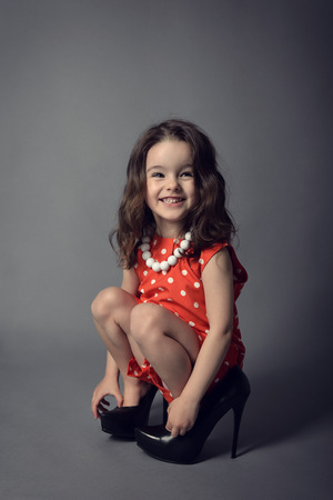 Little fashionista. Little beautiful fashion girl posing in mother's high heels shoes and happy smiling.の写真素材