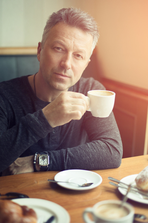 Attractive mid adult man drinking morning coffee in cafe, image toned.の写真素材