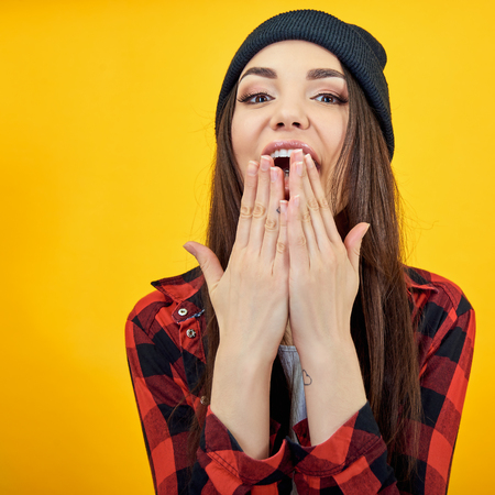 Excited surprised girl cover hands open mouth over yellow background. Emotional female portrait.の写真素材