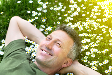 Handsome happy smiling middle-aged man lying on summer meadow green grass with daisyの写真素材