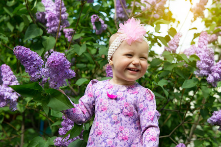 Beautiful little girl appy smiling and smells lilac flowers in spring park. Childhood. Cute kid's face over nature background. Cheerful child's portrait, soft focus.の写真素材