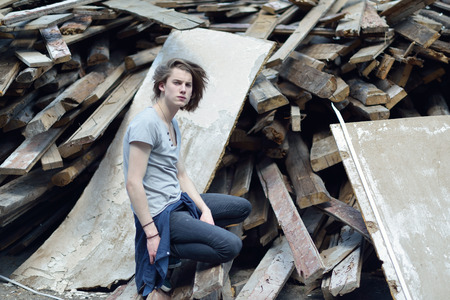 Portrait of young handsome man over wood boards, outdoor. Attractive trendy fashion 18 years old teen boy posing outside over debrisの写真素材