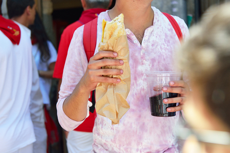 Man in t-short in wine with fast food and wine, San Fermin festival, 06 July 2016, Pamplona, Navarra, Spain.のeditorial素材