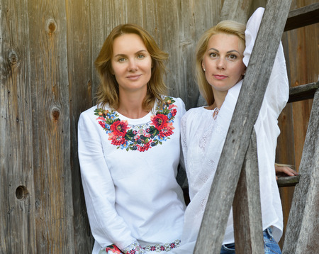 Beautiful ukrainian women posing in traditional clothing vyshyvanka with embroidery over old wooden wall and stairs in Ukrainian villageの写真素材