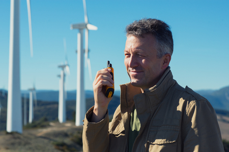 Man talking with portable radio transmitter outdoor over the wind turbines, image toned. Windmill generators. Wind power generators.の写真素材