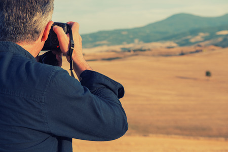 Man professional photographer with digital camera taking photos of fields and moutains, Italy, Tuscany, Europe.の写真素材