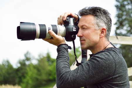 Man professional photographer with digital camera takes photos outdoor. Photo camera in male hands. Destination photographer at work. Paparazzi with telephoto lensの写真素材