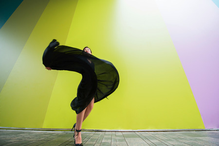 Fashion woman. Young beautiful chinese girl dancing outdoor wearing long black dress with high heels...