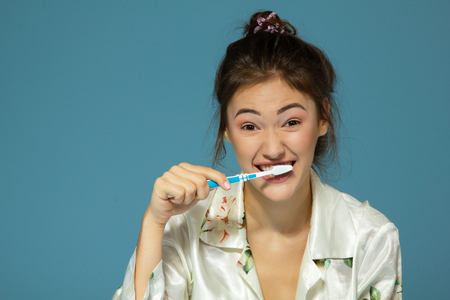 Happy funny teen girl brush her teeth, healthy concept. Morning theme, over blue background.の写真素材