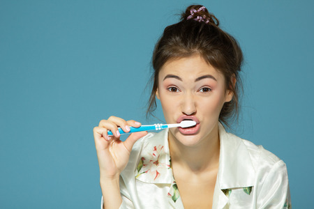 Happy funny teen girl brush her teeth, healthy concept. Morning theme, over blue background.の写真素材