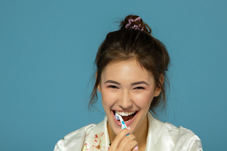 Happy funny teen girl brush her teeth, healthy concept. Morning theme, over blue background.の写真素材