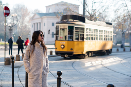 Attractive young woman wearing gray coat with long dark hair and sun glasses posing outdoor in Milan streets, Italy. Beautiful caucasian model portrait. Strit fashionの写真素材