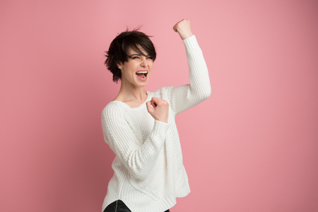Beautiful young woman happy and excited expressing winning gesture. Successful and celebrating victory, triumphant, studio shot over pink backgroundの写真素材