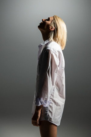 Fashion model. Young blond woman posing in studio wearing white shirt. Beautiful caucasian girl over gray backgroundの写真素材
