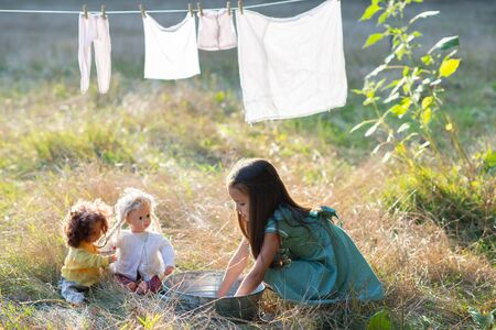 Little girl hangs out to dry retro doll clothes, summer nature outdoor. Washing, children's games, kid's leisure, vintage housework style.の写真素材
