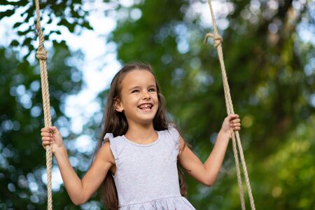 Happy girl rides on a swing in park. Little Princess has fun outdoor, summer nature outdoor....