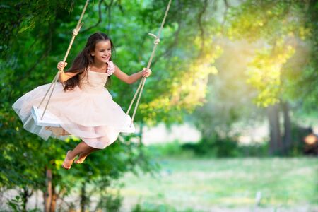 Happy girl rides on a swing in park. Little Princess has fun outdoor, summer nature outdoor. Childhood, child lifestyle, enjoyment, happiness.の写真素材