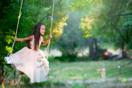 Happy girl rides on a swing in park. Little Princess has fun outdoor, summer nature outdoor. Childhood, child lifestyle, enjoyment, happiness.の写真素材
