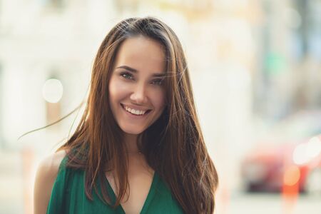 Young pretty likable cheerful woman posing summer city outdoor. Beautiful self-confident girl dressed in emerald-colored jumpsuit with long brown hair walking street enjoing her life, urban lifestyleの写真素材