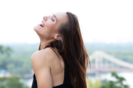 Young pretty likable cheerful woman is laughing summer city outdoor in Kyiv, Ukraine. Beautiful self-confident girl with long brown hair posing on Dnipro river bank enjoing her life. Laughter. Happiness,の写真素材