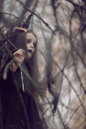 Little girl dressed in a witch costume walking in fall forest with fear expressions. Halloween...
