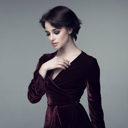 Beauty female portrait. Young attractive woman posing at studio over gray background. Beautiful model with perfect make-up dressed evening burgundy dress looking at camera.の写真素材