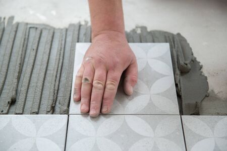 Tiler laying the ceramic tile on the floor. Professional worker makes renovation. Construction....