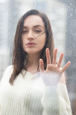 Young beautiful woman with long dark hair dressed in a white sweater, outdoor behind the window pane...