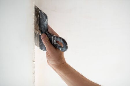 Worker putsty plasterboard ceiling in new appartment, bottom view. Repairman works with plasterboard, plastering dry-stone wall, home improvement. A man makes repairs at house. Putty knife in male hand. Hand workの写真素材