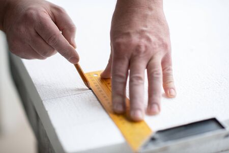 Styrofoam, seiling mounting. A man cuts foam. Warming. Repair in the house. DIY repair. Work with polystyrene foam, insulation of walls and ceiling. Male hands with tools closeupの写真素材