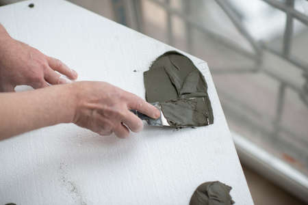 A man putsglue with putty knife on foam to stick it to the ceiling. seiling mounting. A man glues...