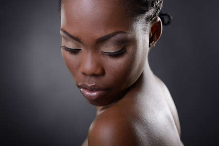 Gorgeous young african american woman looking down st copy space, over black background. Beauty portrait of charming girl with clean skin, studio shotの写真素材