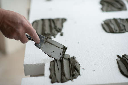 A man putsglue with putty knife on foam to stick it to the ceiling.  seiling mounting. A man glues...