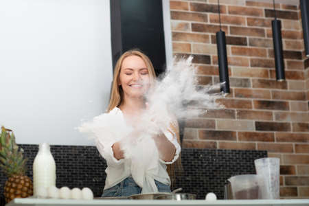 Young woman standing in the kitchen at home and cooking with enjoyment bakery products of flour,...
