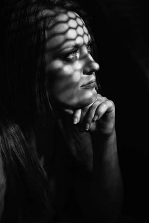 Beautiful woman confesses in the confessional, black and white. Praying woman, fine art portrait with interesting ligth and shadow pattern. Absolution.の写真素材