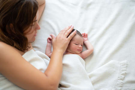 Mother lying in bed with her newborn daughter at home, takes care about baby. Family values,...