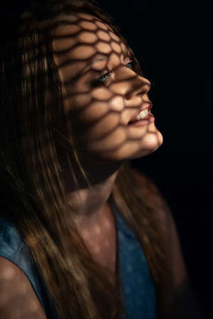 Beautiful woman confesses in the confessional. Praying woman, fine art portrait with interesting ligth and shadow pattern. Absolution.の写真素材