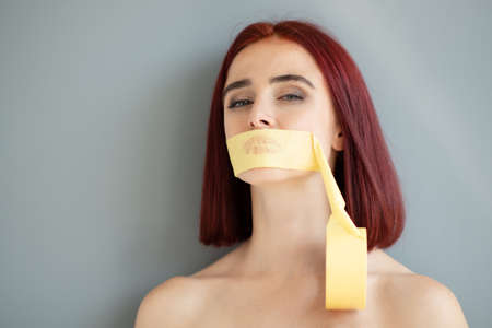 Young pretty woman with a mouth sealed with tape. Silence of social, gender and domestic violence...
