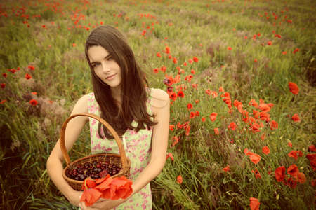 Young beautiful woman holding basket with cherry and strawberry on a poppy field, summer nature outdoor.の写真素材