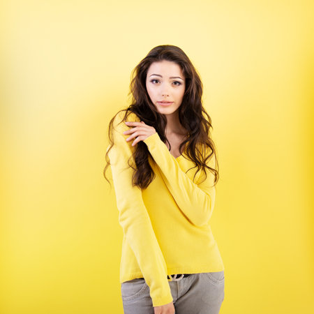 Charming young brunette woman with perfect brown curlyg hair and positive face expression posing at studio over yellow background.の写真素材