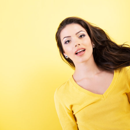 Portrait of beautiful young brunette woman with perfect brown curlyg hair and surprised face expression, over yellow background.の写真素材