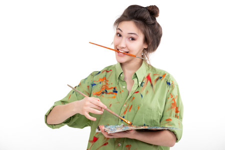 Attractive girl painting with oil paints, professional painter at work over white background. Studio portrait of young woman artistの写真素材